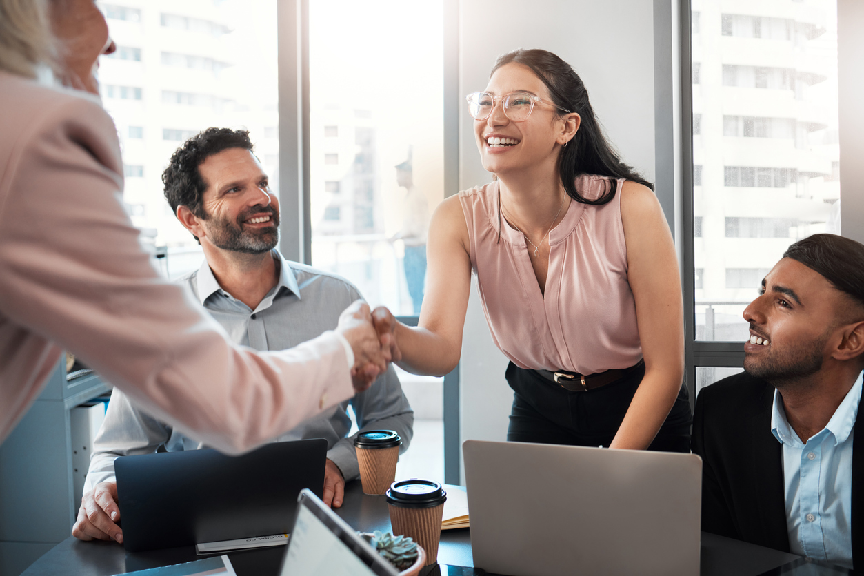 A business development representative shaking hands with a client at a conference table.