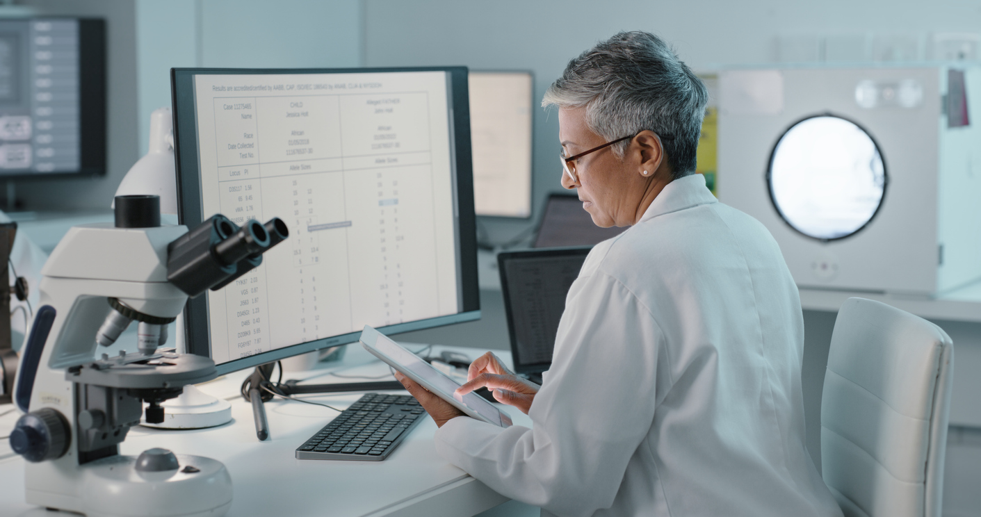 Forensic science technician looking at a tablet and computer in a lab.